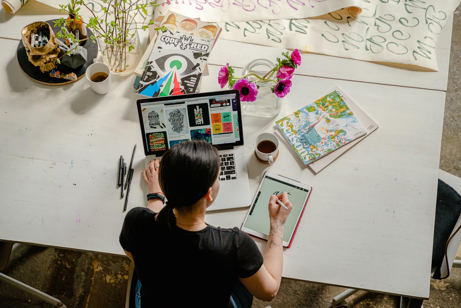 Artist at drawing on a tablet at a desk with a laptop, pencils, books and coffeeArtist at drawing on a tablet at a desk with a laptop, pencils, books and coffee